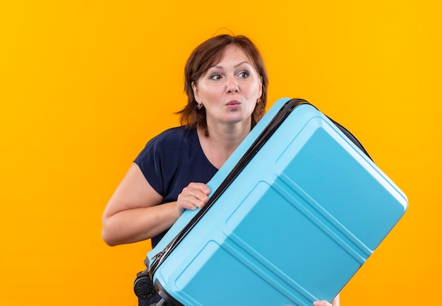 Looking at side concerned middle-aged traveler woman holding suitcase on