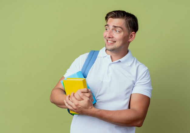 looking at side concerned young handsome male student wearing back bag holding books isolated on olive green background