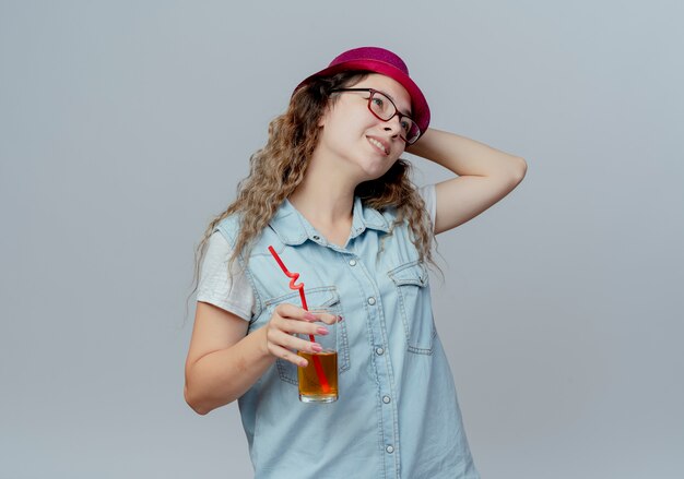 측면을 보면 주스 잔을 들고 흰색 배경에 고립 된 모자에 손을 넣어 분홍색 모자에 어린 소녀 혼란