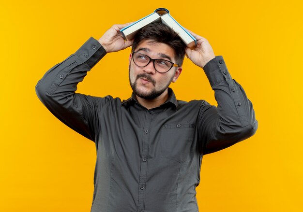 looking at side pleased young businessman wearing glasses covered head with book