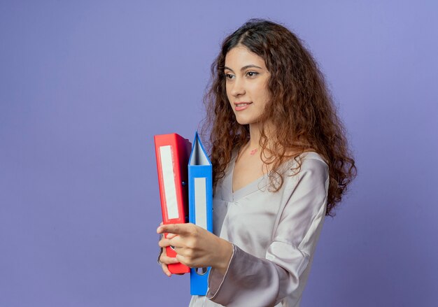 Looking at side pleased young pretty girl holding folders 