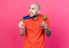 Free photo looking at side pleased young sporty man wearing and holding medal with winner cup