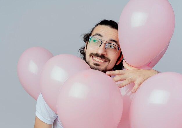 Looking at side smiling handsome man wearing glasses holding balloons 