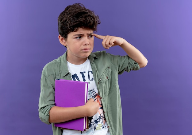 Free photo looking at side thinking little schoolboy holding book and putting finger on head