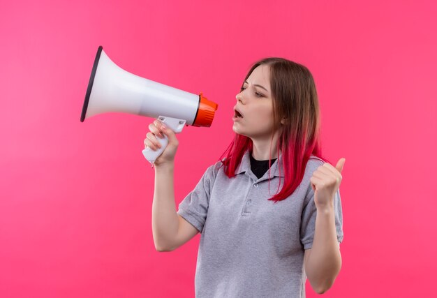 孤立したピンクの背景にスピーカーを通して話す灰色のTシャツを着ている若い美しい少女の側を見て