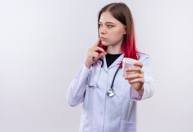 Looking at side young doctor girl wearing stethoscope medical robe holding out empty can to camera on isolated white background