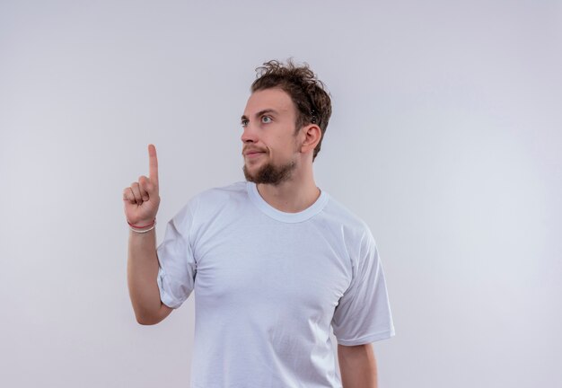 Looking at side young guy wearing white t-shirt points to up on isolated white background