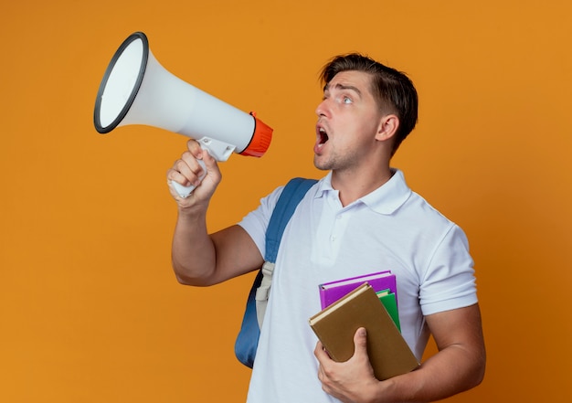 looking at side young handsome male student wearing back bag holding books and speaks on loudspeaker