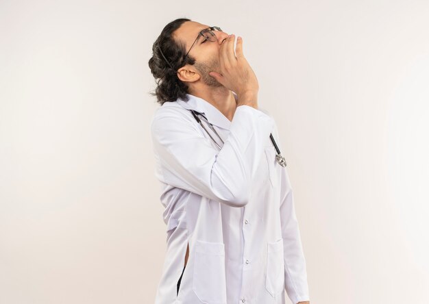 Looking at side young male doctor with optical glasses wearing white robe with stethoscope calling someone
