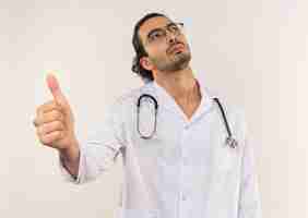 Free photo looking at side young male doctor with optical glasses wearing white robe with stethoscope his thumb up