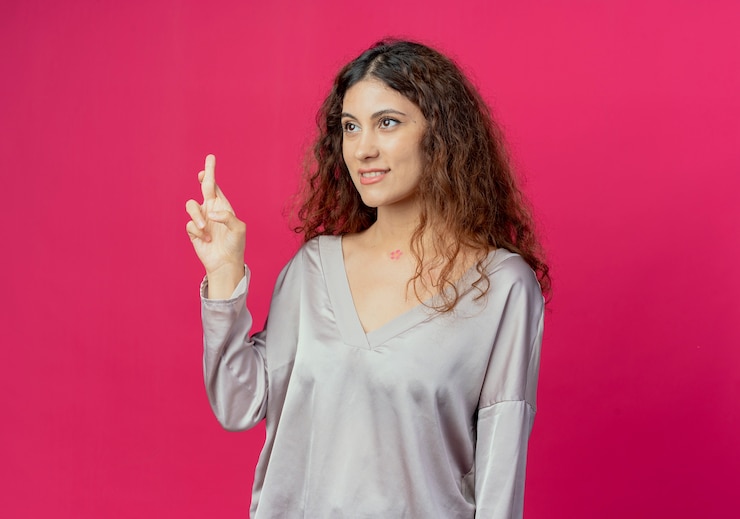 मुफ़्त फोटो looking at side young pretty girl crossing finger isolated on pink background