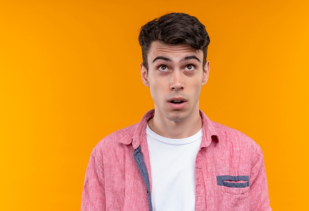 Looking to up caucasian young guy wearing pink shirt on isolated orange background