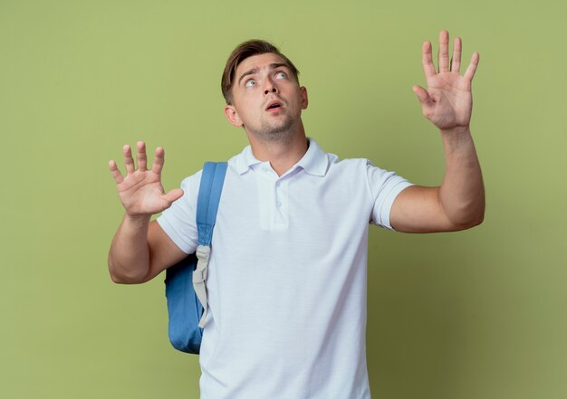 Looking at up concerned young handsome male student wearing back bag spreads hands isolated on olive green background