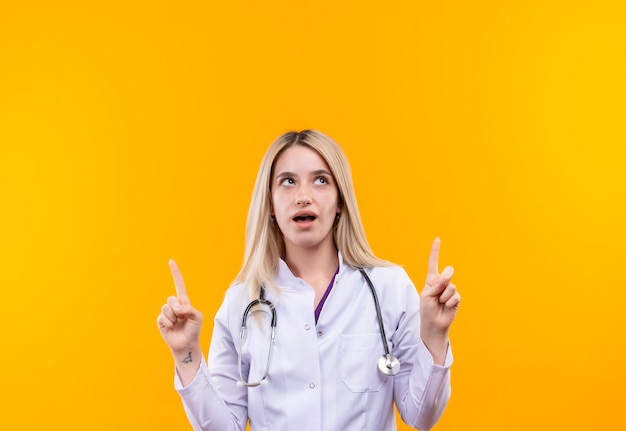 Глядя на доктора, молодая девушка со стетоскопом в медицинском халате указывает на изолированный желтый фон