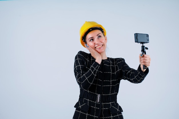 Alzando gli occhi, la ragazza dell'ingegnere sta prendendo selfie con la sua macchina fotografica mettendo la mano sul mento su sfondo bianco