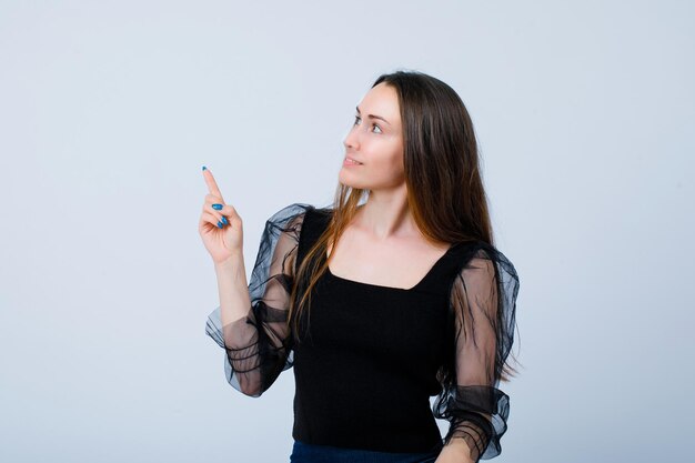 Looking up girl is pointing up with forefinger on white background