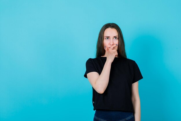 Looking up girl is thinking by putting hand on chin on blue background