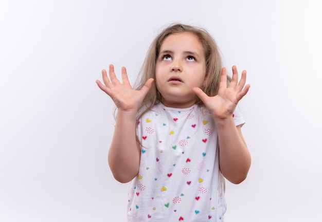 Looking to up little school girl wearing white t-shirt raising hands on isolated white background