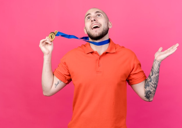 Free photo looking at up smiling young sporty man wearing medal and holding and spread hand