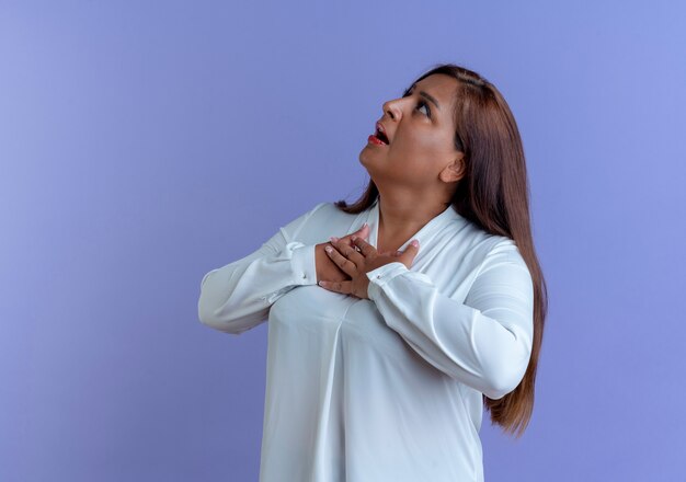 Looking at up surprised casual caucasian middle-aged woman putting hands on heart 