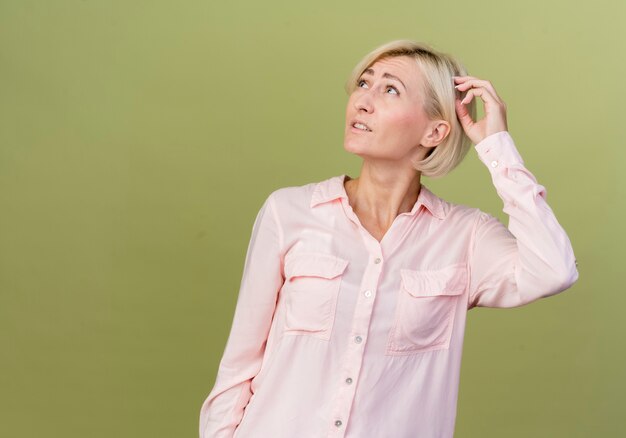 Looking at up thinking young blonde slavic woman putting hand on head 