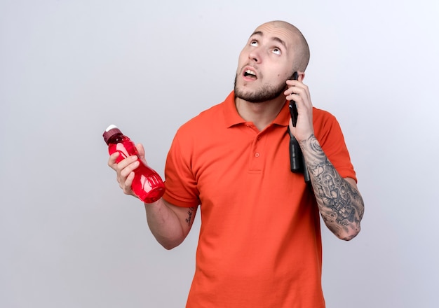Глядя на мыслящего молодого спортивного человека, держащего бутылку с водой и говорящего по телефону