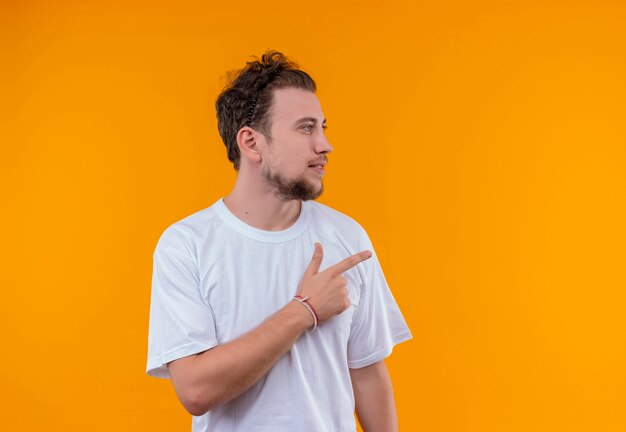 Looking young guy wearing white t-shirt points to side on isolated orange background