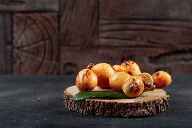 Loquats on a wood slice with leaves side view on a dark textured and wooden background space for text