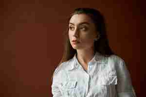 Free photo lose up image of serious attractive young woman with brown hair gathered back thinking about something, having pensive deep in thoughts look, posing isolated