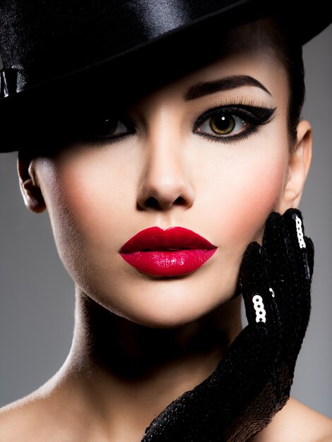 Сlose-up portrait of a woman in a black hat and gloves with red lips posing 