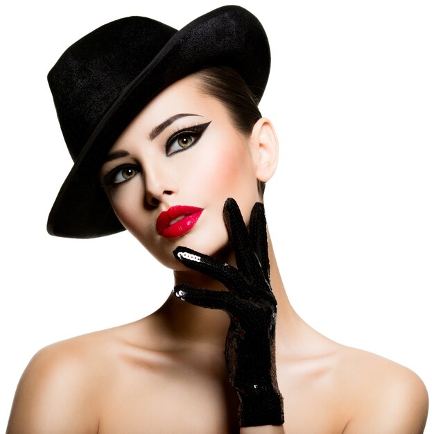Сlose-up portrait of a woman in a black hat and gloves with red lips posit 