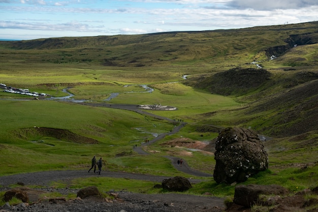 Lot of people walking along a narrow pathway in a green land surrounded by green hills