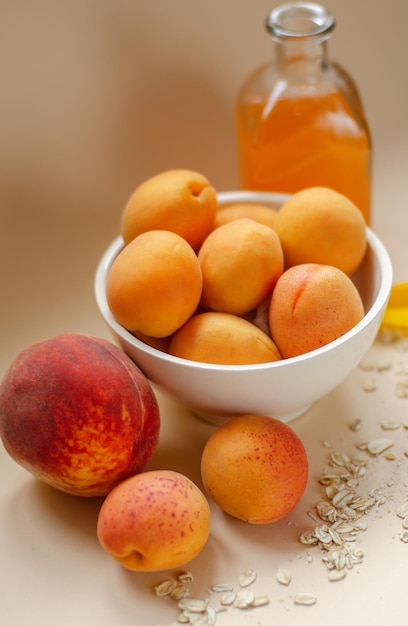 Free photo lots of apricots on a white plate and glass of apricot juice on a white table strewn with oatmeal. summer harvest.