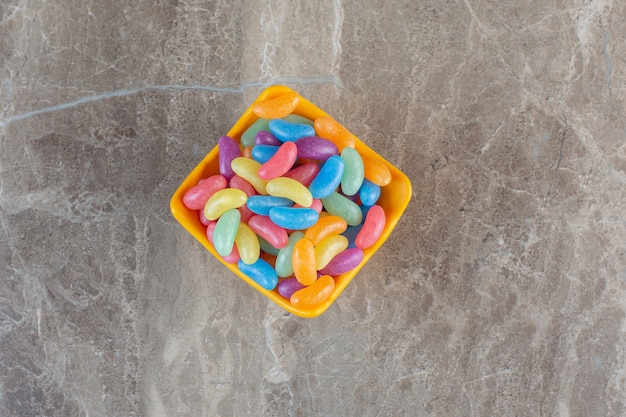 Free photo lots if jellybeans on orange bowl over grey surface.