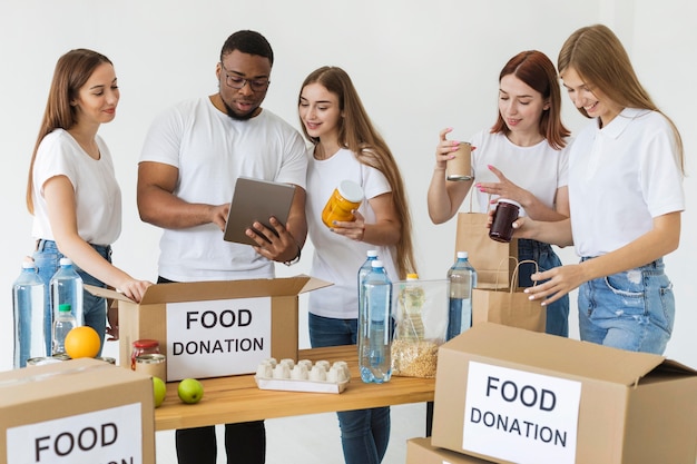 タブレットを使って食料の寄付で箱を準備する多くのボランティア