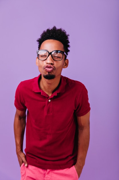 Free photo lovable african man standing on pastel violet wall. dark-haired guy posing with kissing face expression.