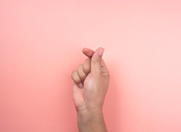 Концепция любви и заботы. рука делает маленькое сердце, изолированные на розовом фоне. жест языка тела символа мини-сердца, сделанный большим и указательным пальцами.