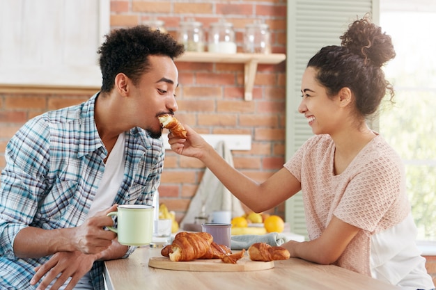 사랑과 배려 개념. 사랑스러운 커플은 함께 즐거워합니다 : 돌보는 여성이 남편에게 크루아상을 먹이고,