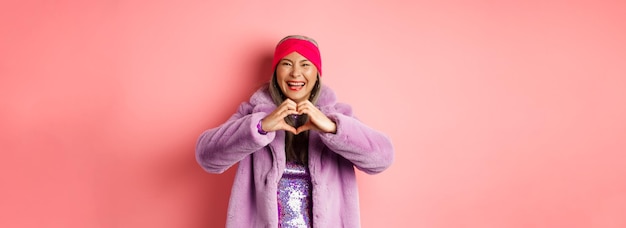 Free photo love and fashion concept happy asian senior female showing heart sign and smiling at camera i love y