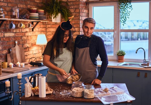 愛とハロウィーンのコンセプト。朝のロフトスタイルのキッチンで一緒に朝食を調理するメイクアップと魅力的なカップル。