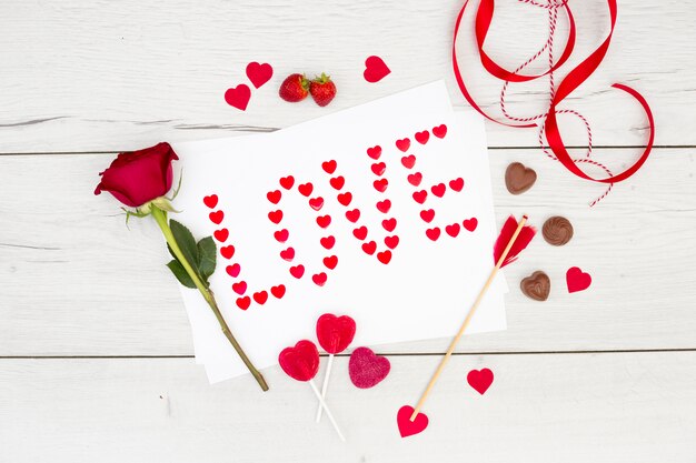 Love inscription on paper near chocolate hearts, ribbon and flower 