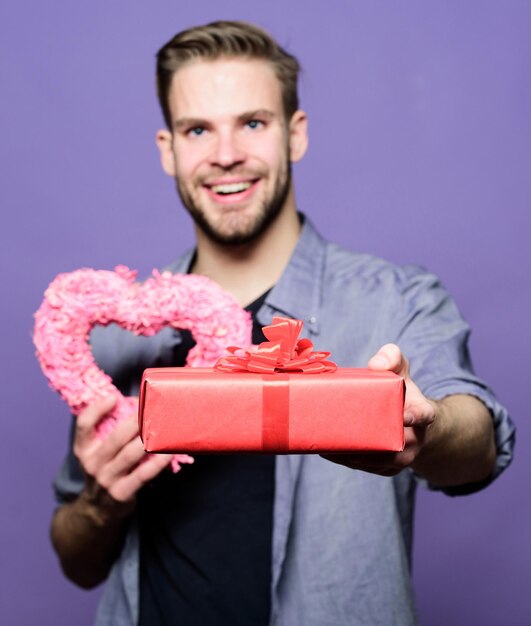 Love and romantic feelings concept. valentines day gift. romantic gift. man with beard and happy face celebrate valentines day. gift for girlfriend. hipster hold gift box and heart violet background.