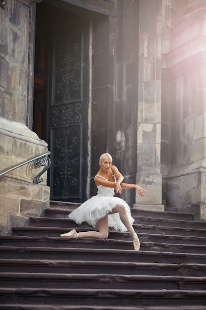그녀의 춤을 보는 것을 좋아합니다. 오래된 건물의 계단에 서서 무릎을 꿇고 포즈를 취한 발레리나의 소프트 포커스 샷