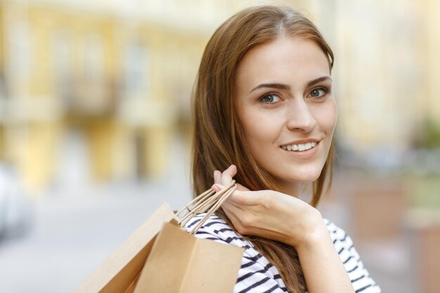 Люблю шопинг Крупный план красивой темноволосой женщины, улыбающейся в камеру с покупками в руке