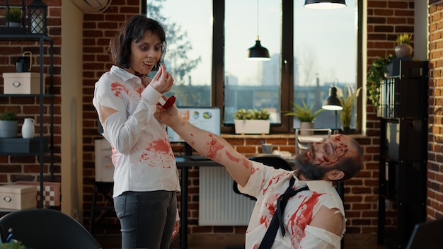 Free photo in love spooky romantic brain-eating zombie man proposing to his creepy girlfriend. two apocalyptic undead monsters with deep bloody wounds getting married in office workspace.