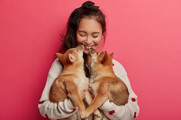 사랑, 부드럽고 따뜻한 느낌과 말이없는 이해. 쾌활한 한국 여성은 혈통 강아지 두 마리로부터 키스를 받고, 애완 동물 없이는 삶을 상상할 수 없으며, 동물 친한 친구와 즐거운 시간을 보냅니다.