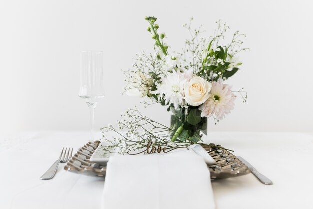 Love text on plate near bunch of flowers and wineglass on white table