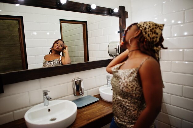 Прекрасная африканская американка с дредами в леопардовой одежде смотрит в зеркало в туалетном кафе Красивая крутая модная черная молодая девушка в помещении