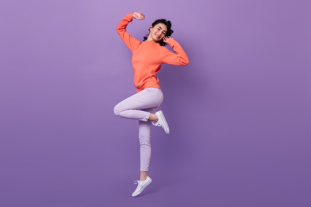 Прекрасная азиатская женщина, стоящая на одной ноге. Вид в полный рост привлекательной стильной японки, прыгающей на фиолетовом фоне.
