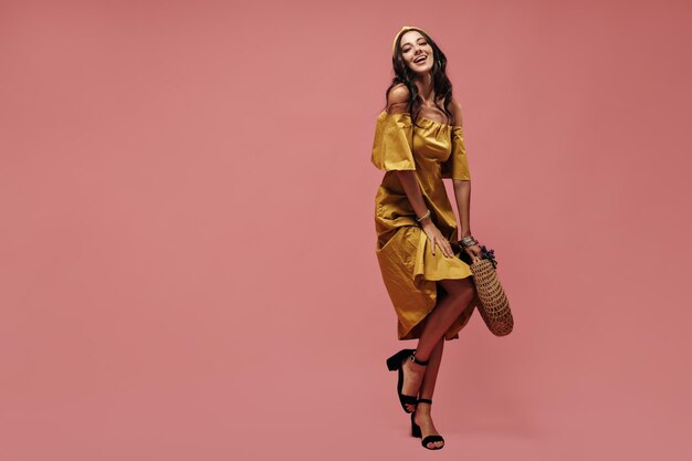 Lovely beautiful lady with wavy hairstyle in modern yellow dress and black stylish heels laughing and looking into camera